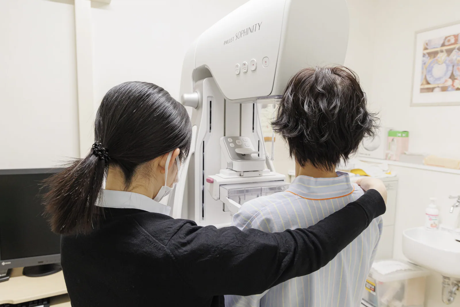 マンモグラフィ装置の前で、技師が受診者の姿勢を整えている様子
